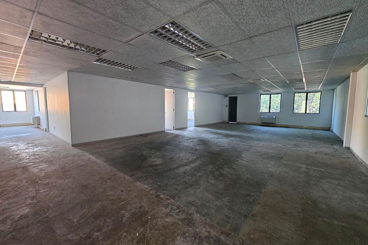 A large, vacant open-plan office space featuring a suspended ceiling with recessed lighting, HVAC units, and large windows, ready for custom flooring and fit-out.