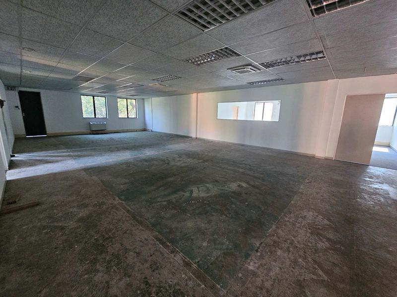 Spacious, empty office area featuring a suspended ceiling, recessed lighting, air conditioning unit, and exposed concrete flooring ready for refurbishment.