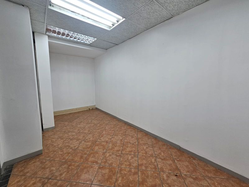 An empty, functional office space featuring ceramic tile flooring, a suspended ceiling with integrated fluorescent lighting, and neutral wall finishes.