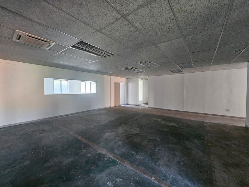 An empty, open-plan office space featuring a suspended ceiling with integrated lighting and air conditioning, and unfinished concrete flooring.