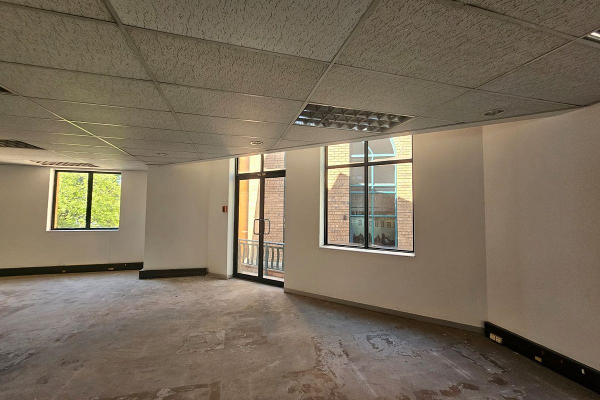 An empty office space featuring a suspended ceiling, recessed lighting, and large windows providing natural light, ready for refurbishment or custom fit-out.