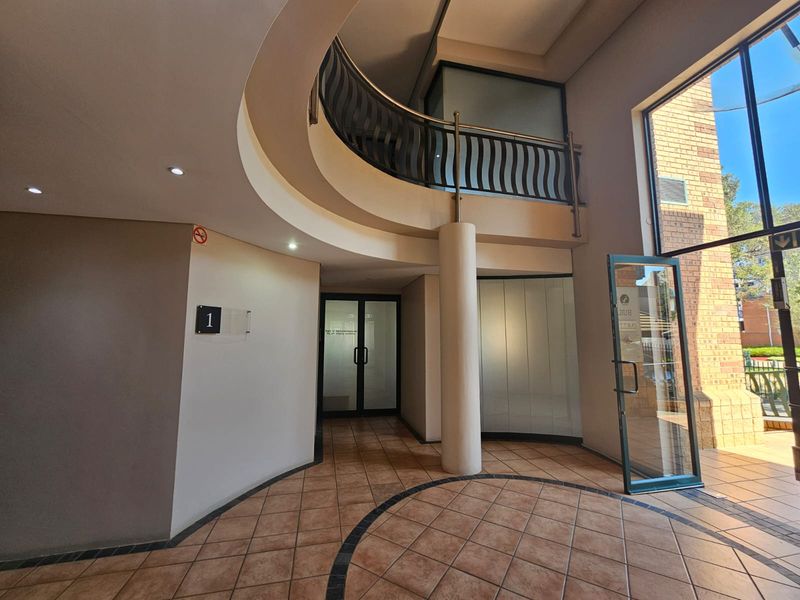 Spacious commercial building entrance featuring a curved mezzanine level, tiled flooring, and large glass doors providing ample natural light.