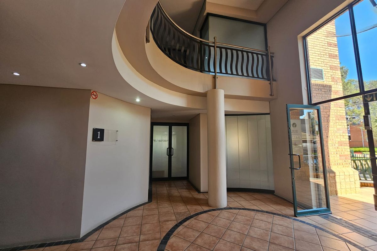 Spacious commercial building entrance featuring a curved mezzanine level, tiled flooring, and large glass doors providing ample natural light.