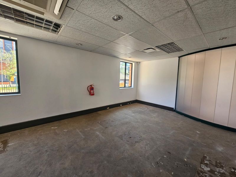 An empty office space featuring a suspended ceiling, recessed lighting, and a partition wall, requiring flooring updates.