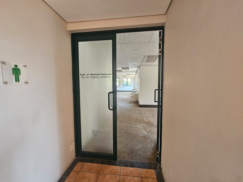 Entrance area leading into an open-plan office space with a glass door, suspended ceiling, and tiled flooring.