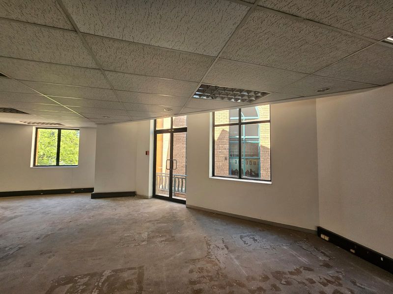 An empty office space featuring a suspended ceiling, recessed lighting, and large windows providing natural light, ready for refurbishment or custom fit-out.