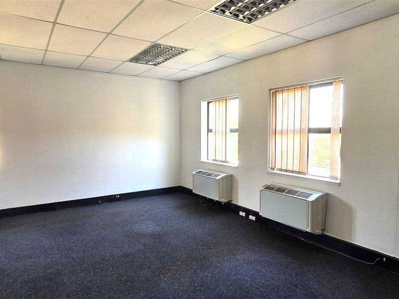 A vacant office space featuring carpeted flooring, suspended ceilings with recessed lighting, and multiple windows equipped with vertical blinds and wall-mounted HVAC units.