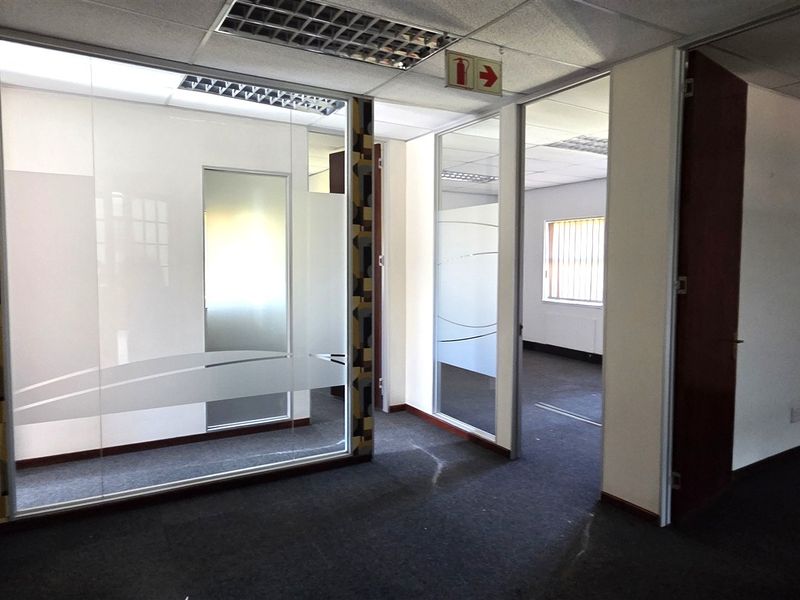 Professional office space featuring glass partitioning, suspended ceilings with recessed lighting, and carpeted flooring, offering a clean and functional layout for business operations.