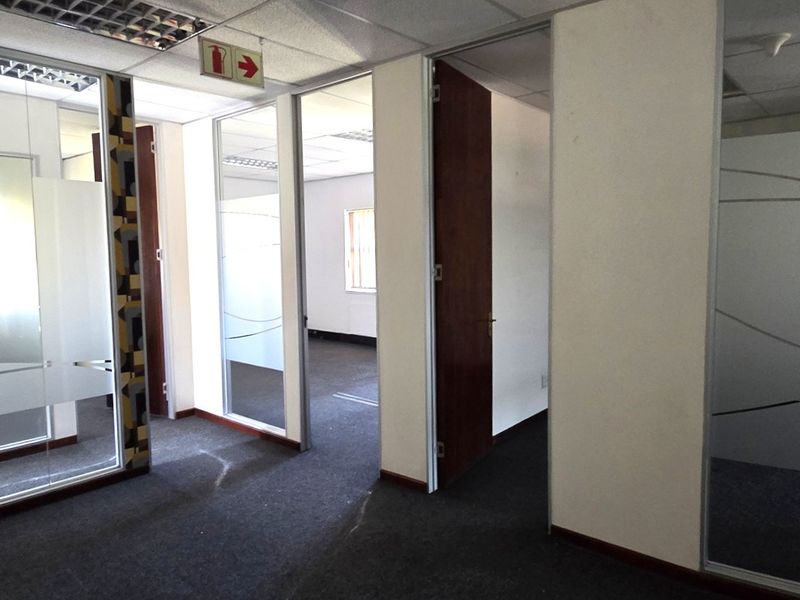 A vacant office suite featuring glass partitions, suspended ceilings with recessed lighting, and carpeted flooring, offering a professional and flexible workspace layout.