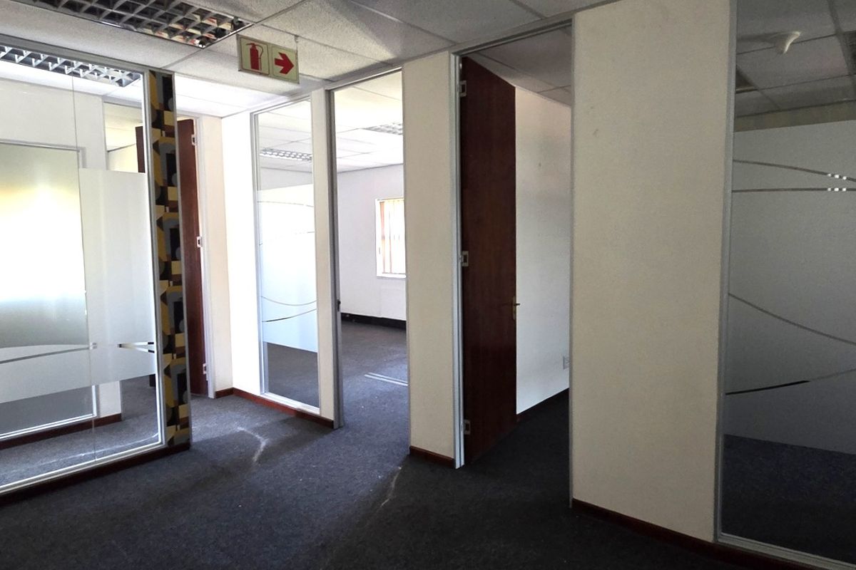 A vacant office suite featuring glass partitions, suspended ceilings with recessed lighting, and carpeted flooring, offering a professional and flexible workspace layout.