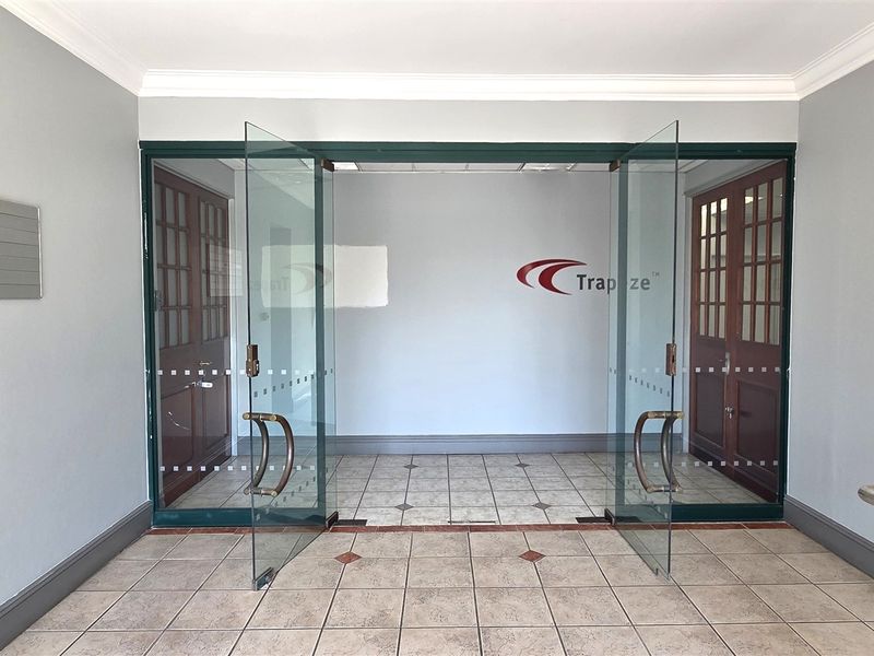 A professional office entrance featuring glass double doors, ceramic tiled flooring, and clear corporate signage in a well-maintained lobby area.