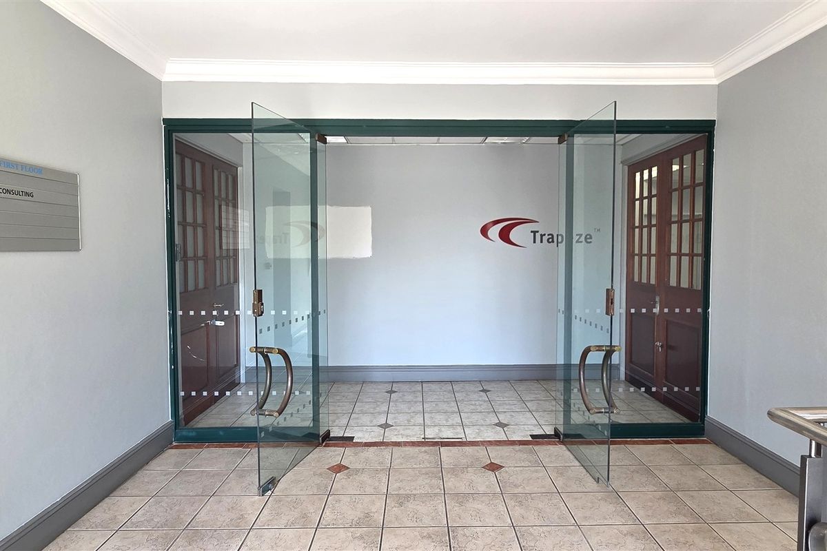 A professional office entrance featuring glass double doors, ceramic tiled flooring, and clear corporate signage in a well-maintained lobby area.