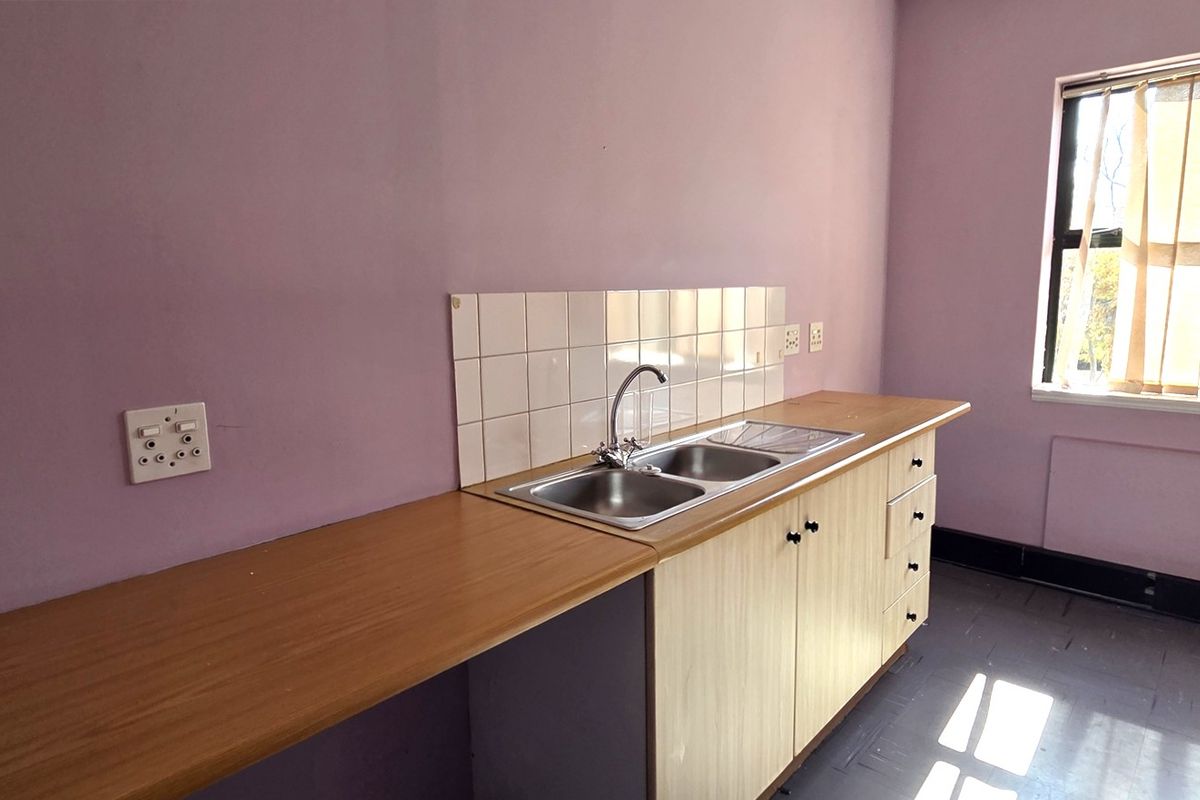 A functional office kitchenette featuring a stainless steel double sink, laminate countertop, tiled splashback, and built-in storage cabinetry.