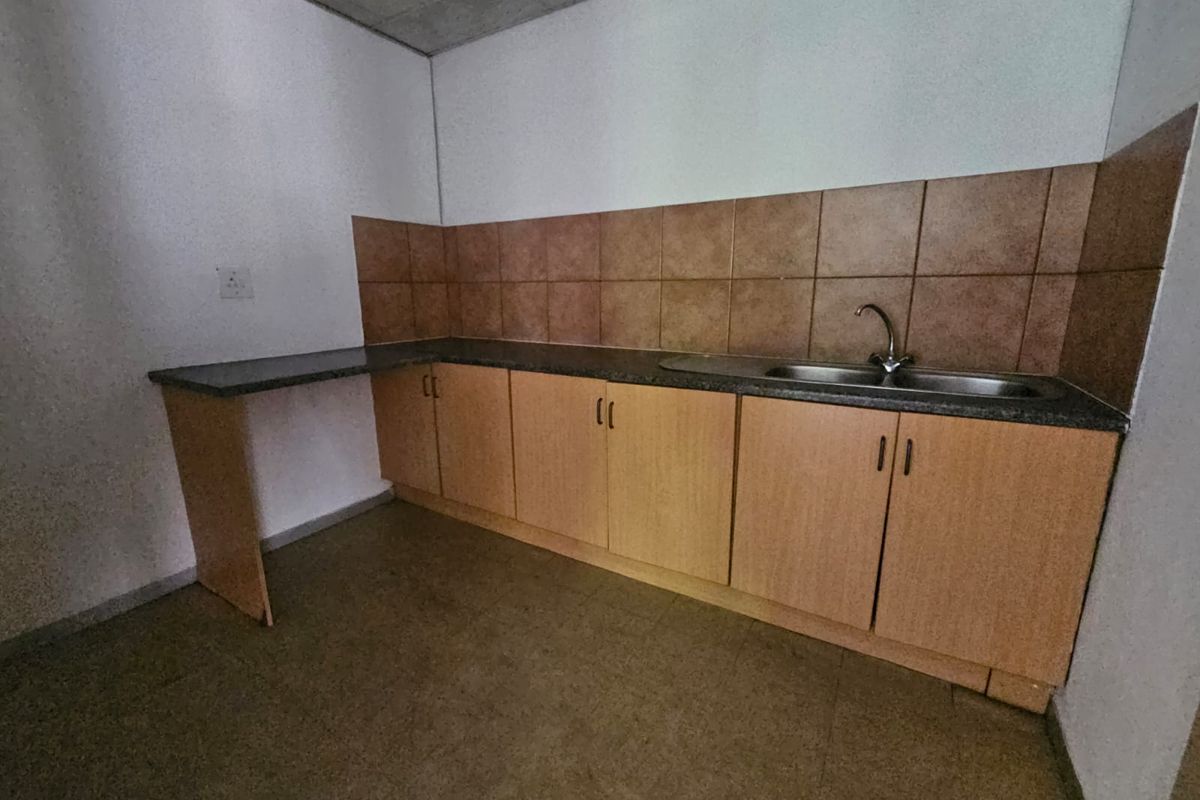 A compact, empty kitchen area featuring laminate cabinetry, a stainless steel sink, and tiled splashbacks, offering a functional space ready for updates.