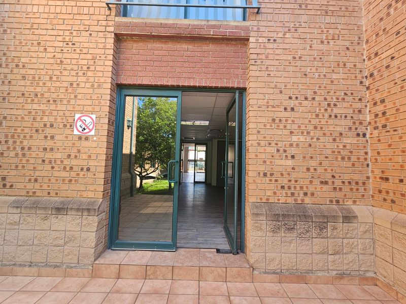Exterior view of a commercial building entrance featuring face brick facade, tiled step, and aluminium framed glass double doors leading into an open interior space.