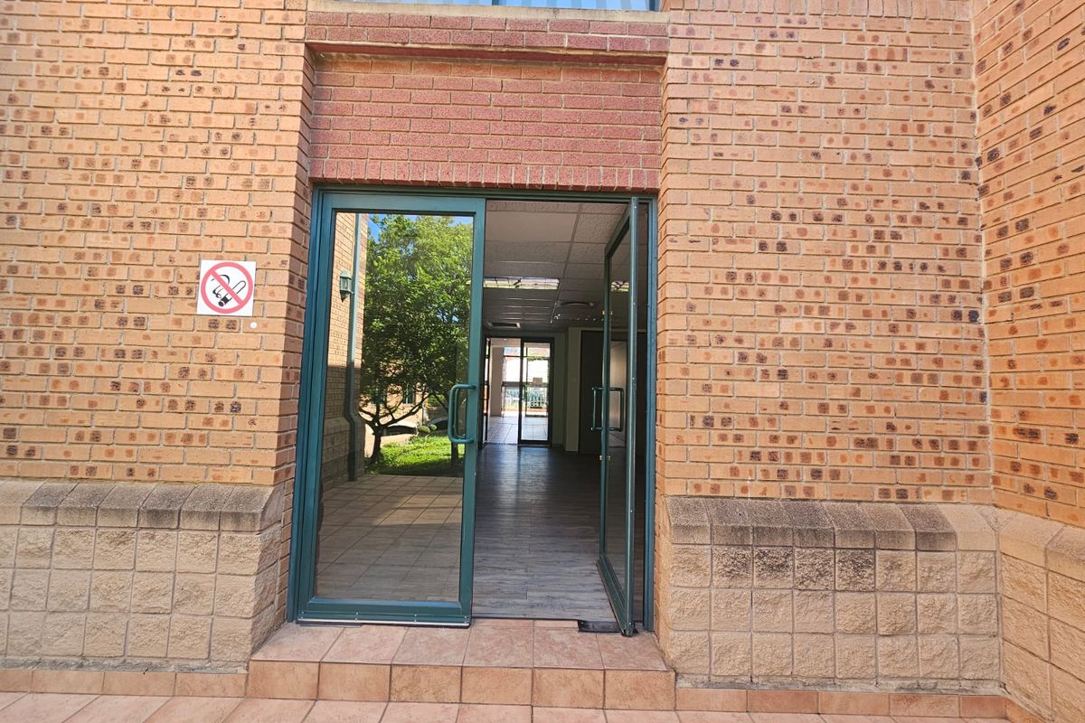 Exterior view of a commercial building entrance featuring face brick facade, tiled step, and aluminium framed glass double doors leading into an open interior space.
