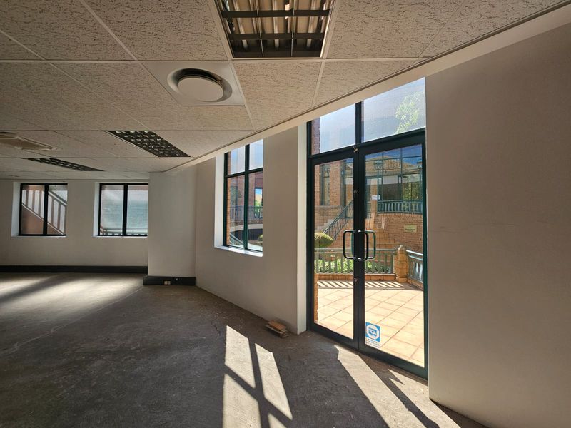 An empty, open-plan office space featuring suspended ceilings, recessed lighting, and large glass doors leading to an outdoor patio area.