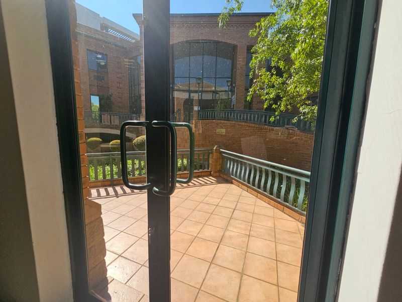 A view from a doorway onto a tiled patio balcony featuring a metal balustrade and overlooking a brick-faced courtyard area.