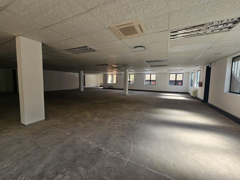 A large, open-plan office space featuring a suspended ceiling, recessed lighting, ducted air conditioning, and exposed concrete flooring.