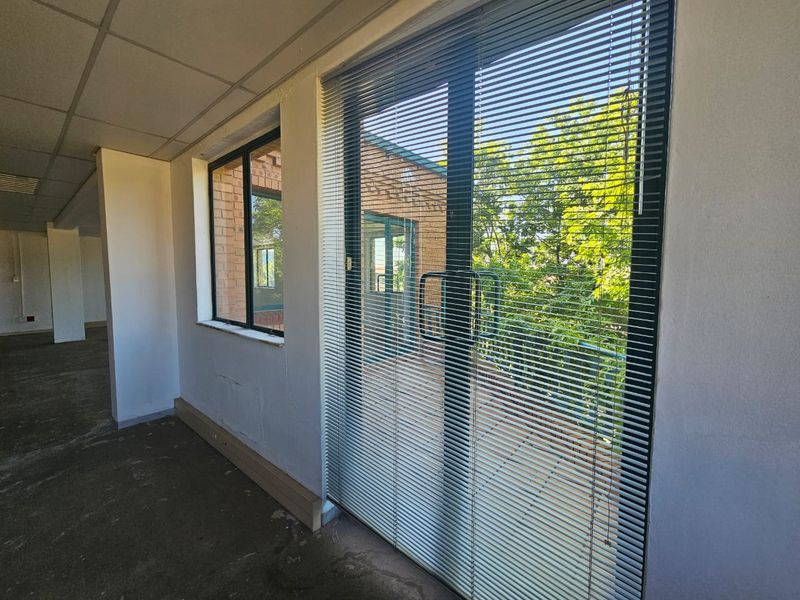 Empty office space featuring a suspended ceiling, concrete flooring, and sliding door access to an outdoor balcony area with venetian blinds.