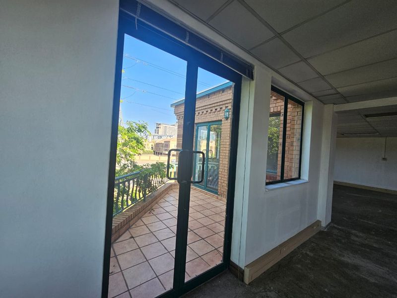 An empty office space featuring a tiled balcony with metal railings, accessible through sliding glass doors, offering an outdoor connection.