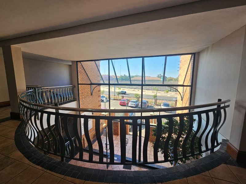 A bright, open-plan landing area featuring a curved metal balustrade and expansive glass windows overlooking the exterior parking area.