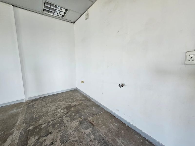 An empty office space featuring exposed concrete flooring, suspended ceiling with recessed lighting, and wall-mounted electrical points, ready for refurbishment.