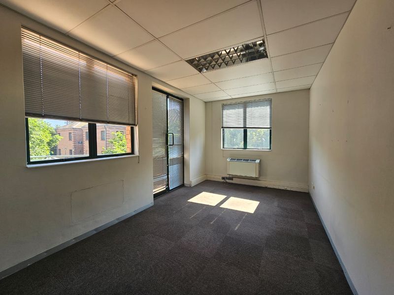 Empty office space featuring carpeted flooring, suspended ceiling with recessed lighting, wall-mounted air conditioning, and access to a balcony via sliding glass doors.