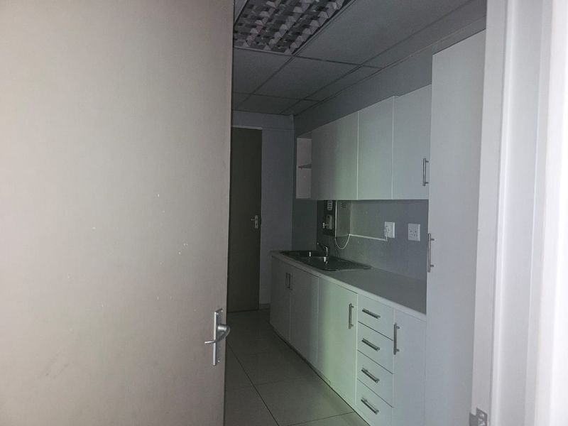 A functional kitchenette area featuring white built-in cabinetry, a stainless steel sink, and tiled flooring, suitable for office or utility use.