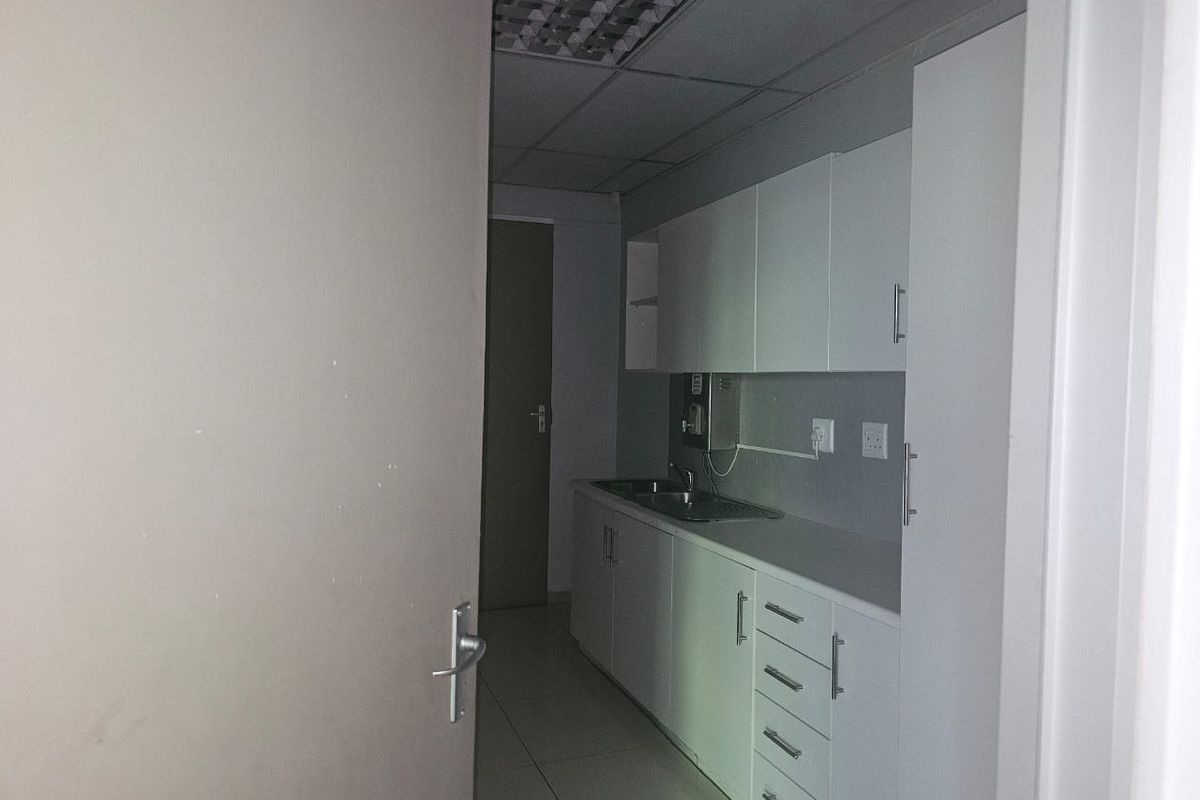 A functional kitchenette area featuring white built-in cabinetry, a stainless steel sink, and tiled flooring, suitable for office or utility use.