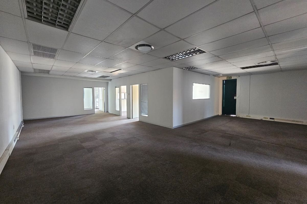 Spacious open-plan office area featuring suspended ceilings, recessed lighting, and carpeted flooring, offering a versatile layout for various business configurations.