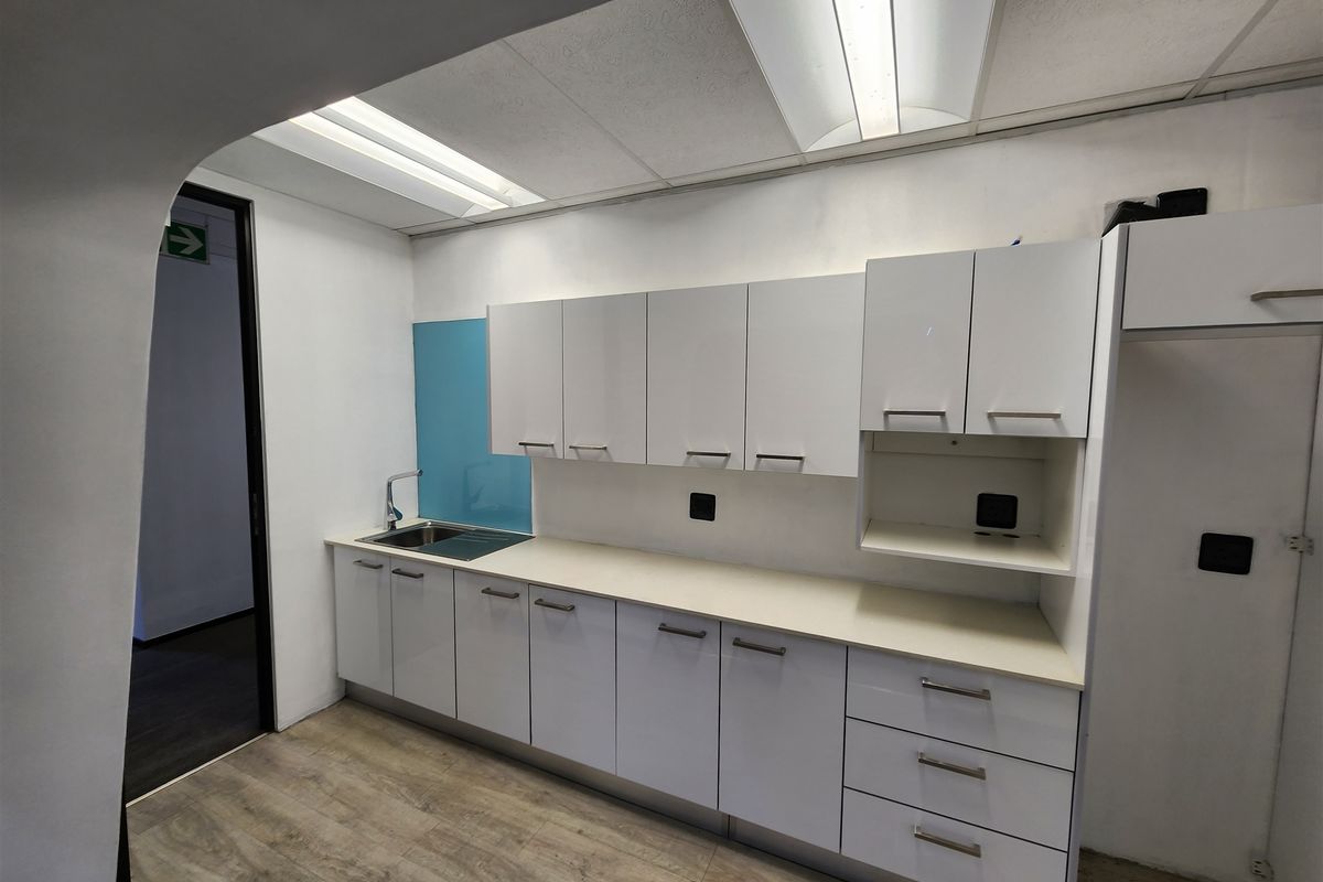 A clean, functional office kitchenette featuring white built-in cabinetry, a stainless steel sink, and modern laminate flooring.