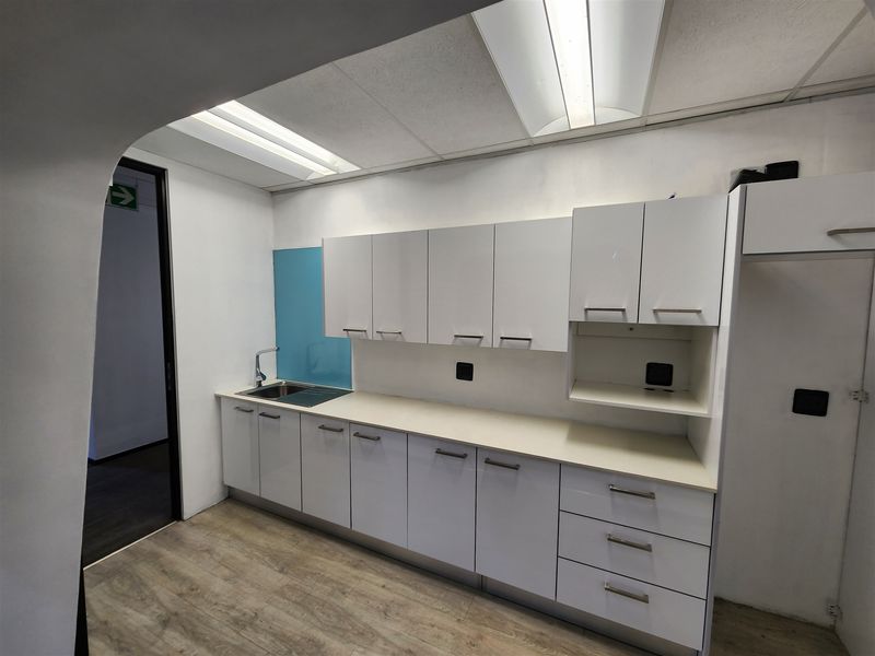 A clean, functional office kitchenette featuring white built-in cabinetry, a stainless steel sink, and modern laminate flooring.