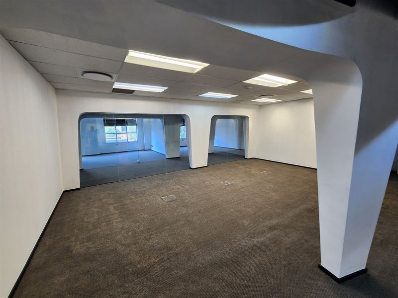 An open-plan office space featuring carpeted flooring, suspended ceilings with recessed lighting, and modern glass partitions creating distinct work areas.