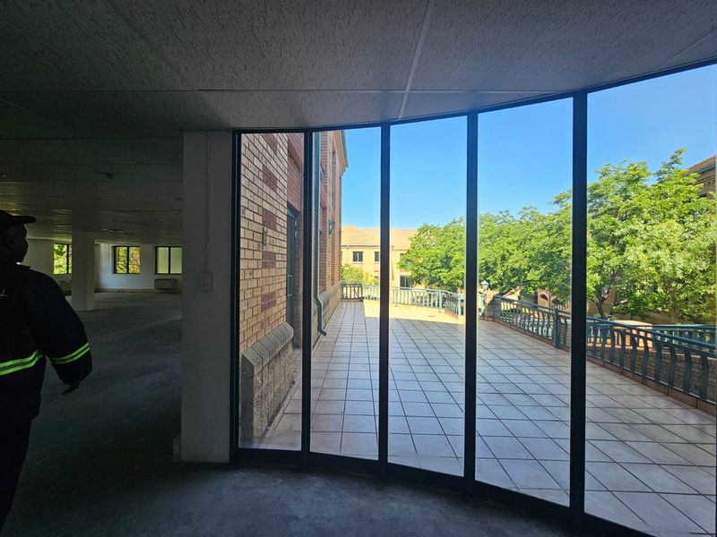 Spacious open-plan interior featuring curved floor-to-ceiling windows that open onto a tiled balcony with metal balustrades, offering a bright and airy workspace.
