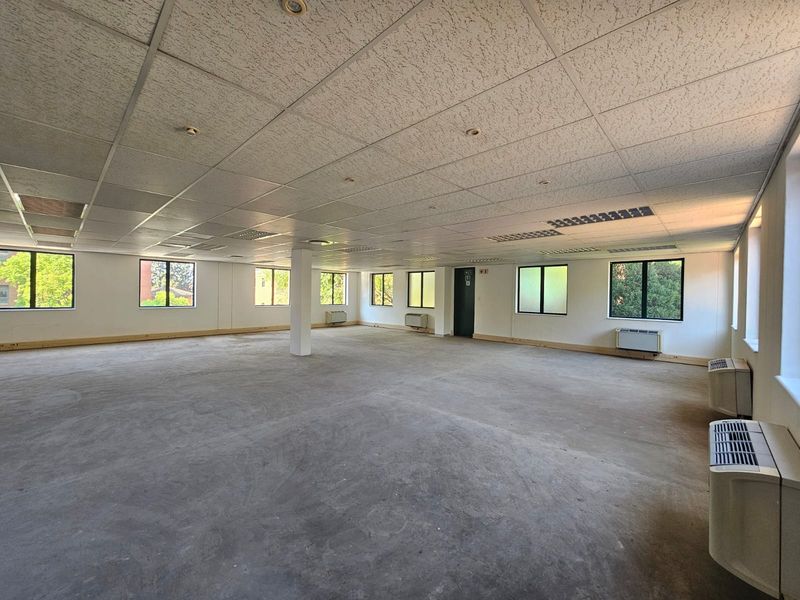 Spacious open-plan office area featuring a suspended ceiling, recessed lighting, multiple windows, and wall-mounted air conditioning units, currently in a shell condition.