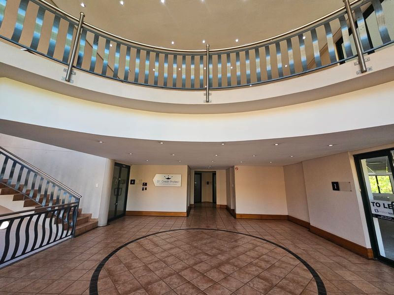 Spacious commercial building entrance foyer featuring a circular tiled floor design, stainless steel balustrades, and recessed ceiling lighting.