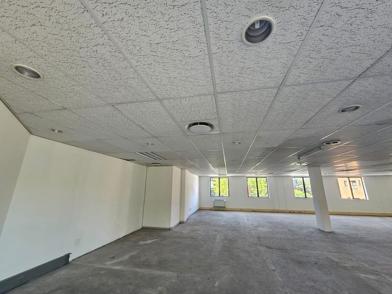 Spacious open-plan office area featuring a suspended ceiling, recessed lighting, and large windows, currently awaiting final flooring installation.