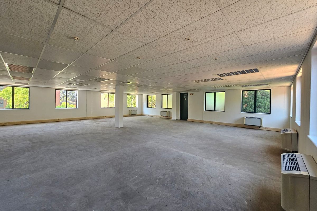 Spacious open-plan office area featuring a suspended ceiling, recessed lighting, multiple windows, and wall-mounted air conditioning units, currently in a shell condition.