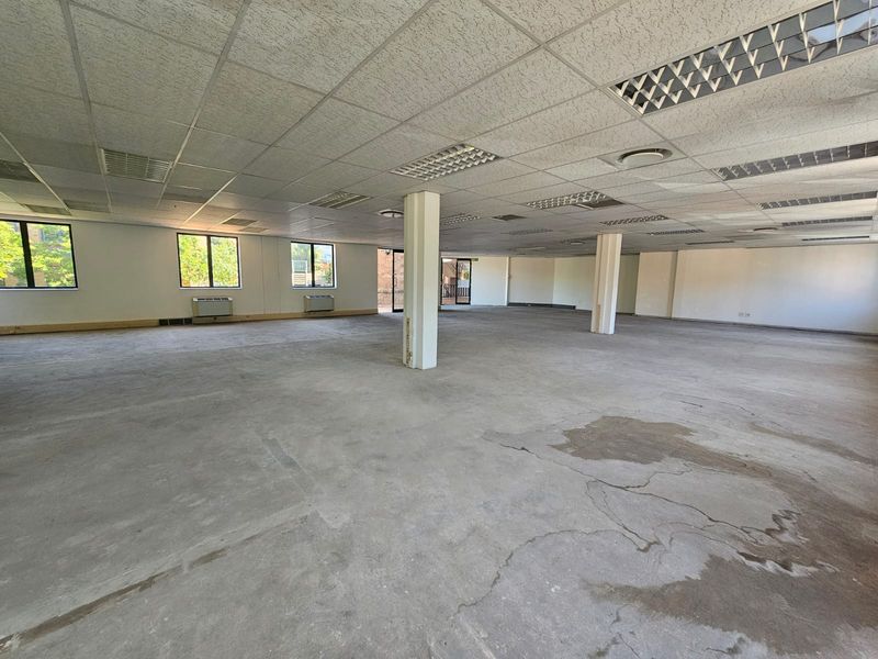 Spacious open-plan office area featuring a suspended ceiling, recessed lighting, and large windows, currently awaiting flooring installation and final finishes.