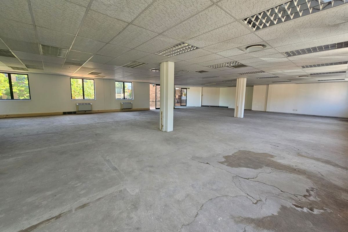 Spacious open-plan office area featuring a suspended ceiling, recessed lighting, and large windows, currently awaiting flooring installation and final finishes.