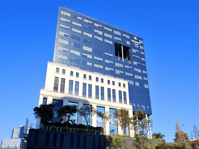 A modern high-rise office building featuring a striking combination of glass curtain walling and stone-clad architectural elements under a clear blue sky.