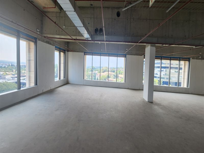 An open-plan office space in shell condition featuring exposed concrete ceilings, large windows with natural light, and panoramic views.