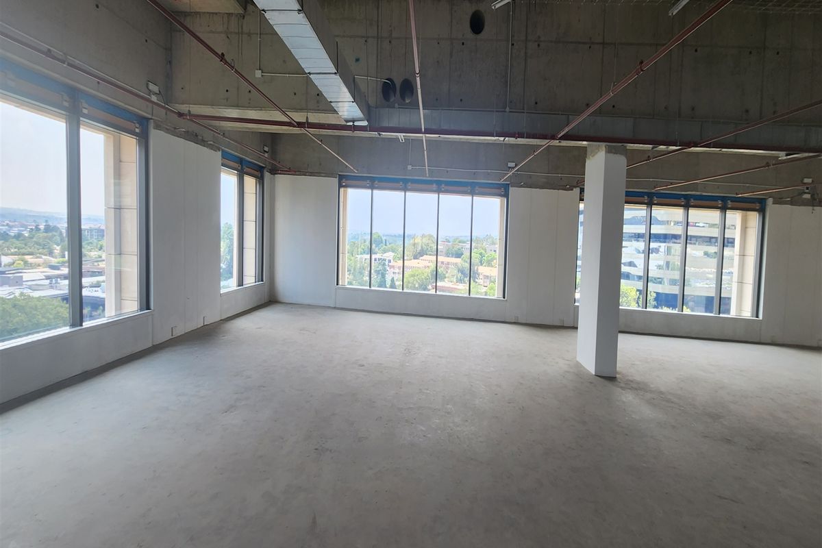 An open-plan office space in shell condition featuring exposed concrete ceilings, large windows with natural light, and panoramic views.