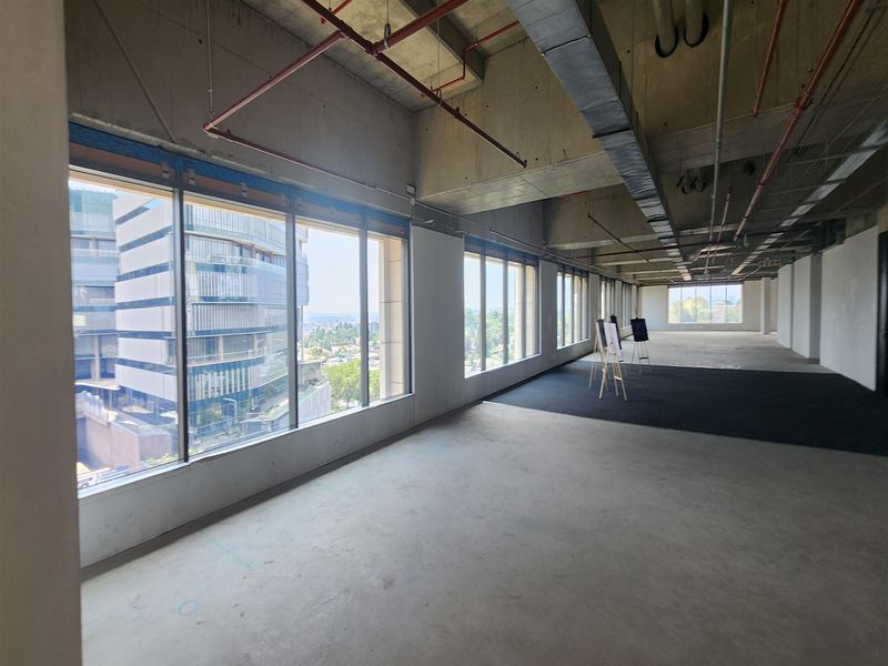 An expansive, open-plan office space featuring industrial-style exposed ceilings, concrete floors, and large windows providing ample natural light and urban views.