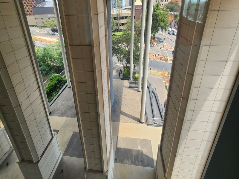 Elevated view of a modern office building entrance featuring stone-clad columns and a paved pedestrian plaza area.