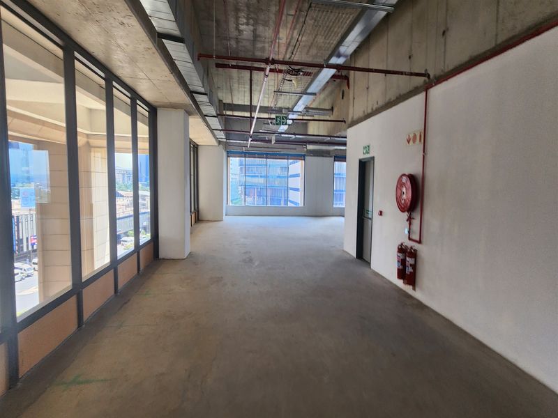 An open-plan office space featuring industrial-style exposed concrete ceilings, large windows providing natural light, and essential fire safety equipment installed.