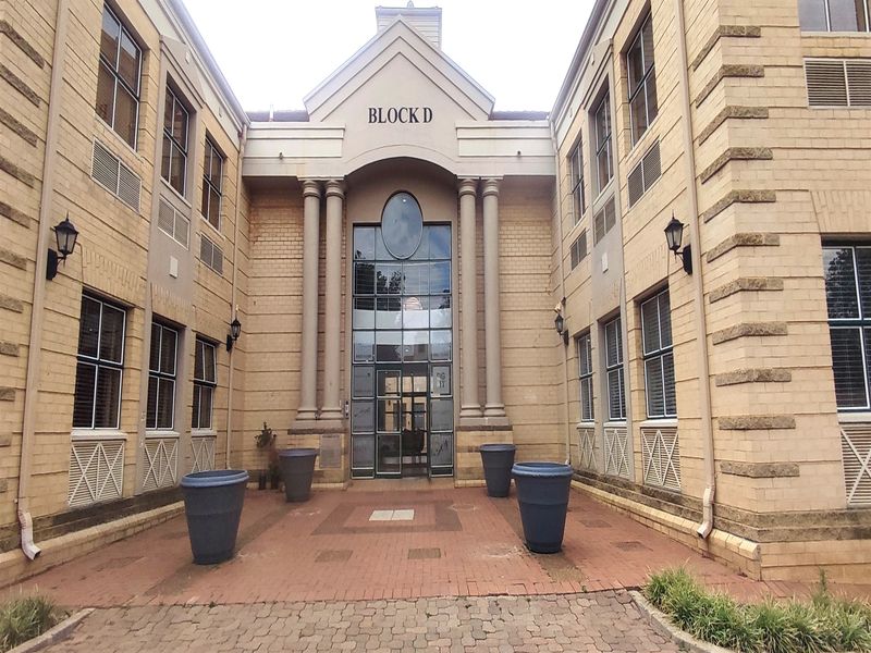 Front entrance facade of Block D office building featuring a brick exterior, decorative columns, and a central glass entryway with paved courtyard access.