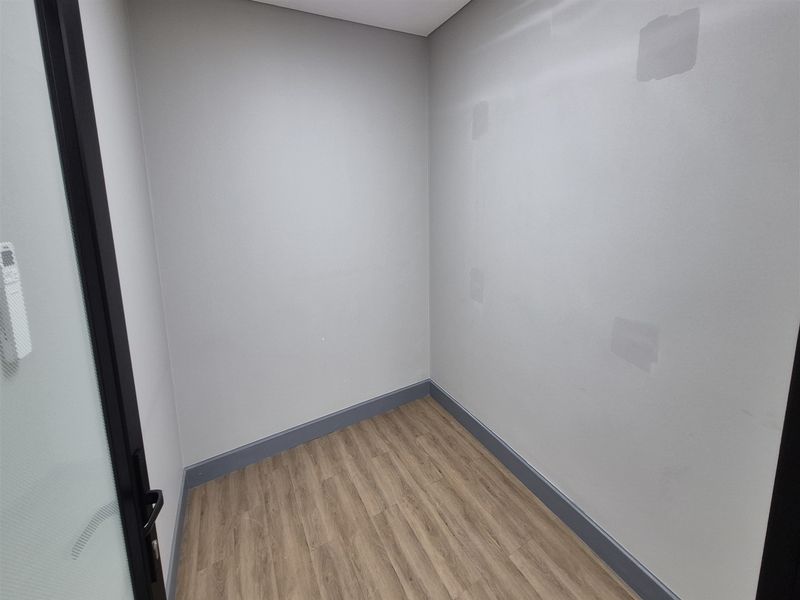 A vacant office space featuring wood-look laminate flooring, grey skirting boards, and a modern glass-panelled door, ready for professional fit-out.