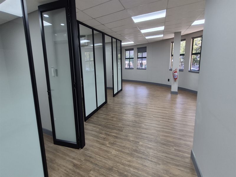 Modern open-plan office space featuring glass partition walls, wood-look vinyl flooring, and recessed ceiling lighting, providing a bright and professional work environment.